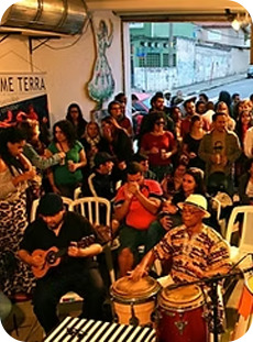 Evento cultural com músicos tocando instrumentos de percussão e cordas em um espaço comunitário repleto de participantes.
