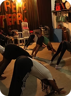 Grupo de pessoas participando de uma prática corporal em um espaço cultural com decoração simples.