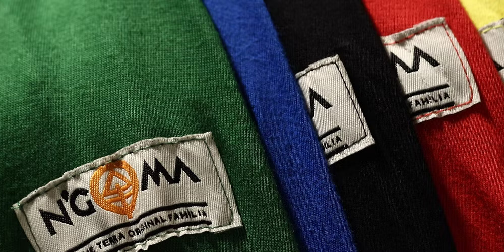 Tecidos coloridos em verde, azul, preto, vermelho e amarelo, com etiquetas da marca N'Goma em destaque.