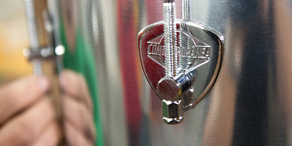 Detalhe de um tambor de percussão com a marca "Contemporânea" visível na placa metálica.