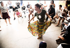 Participante em workshop de dança, girando com saia colorida enquanto o público observa.