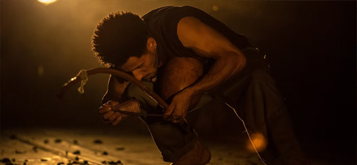 Artista em performance intensa segurando um berimbau em um palco com iluminação dramática.